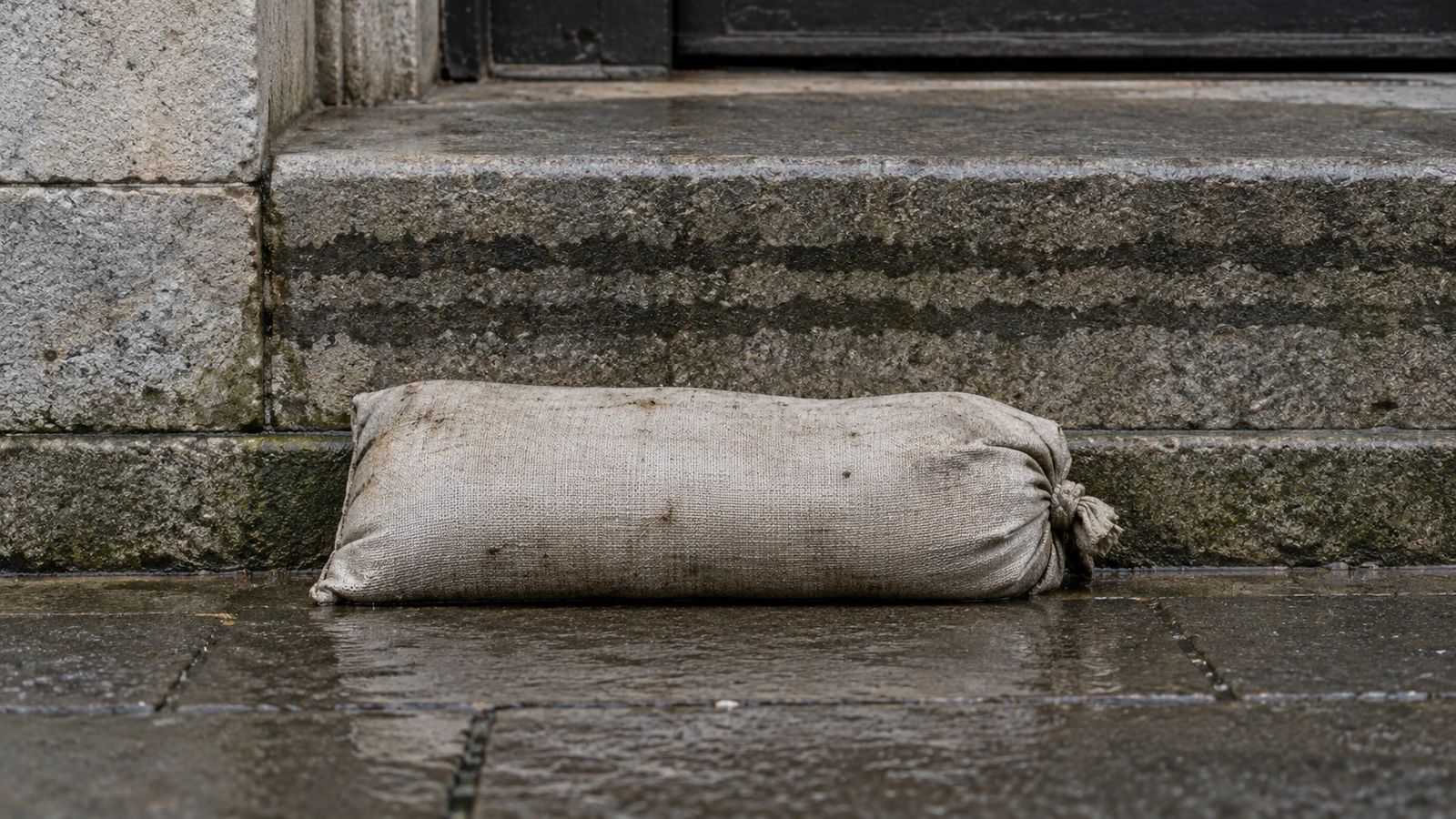 A sandbag against a stone step, with old water stains on the stone above it